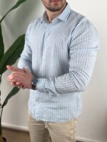 Svetlo plava prugasta muška lanena košulja u kontrastu sa drvenim okolinom