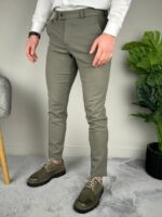 Bočni profil maslinaste elegantne muške pantalone, opušten stav uz zelenu biljku i sivu fotelju