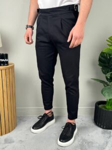 Model u crnim elegantnim muškim pantalonama sa podesivim pojasom, frontalni stav uz beli zid