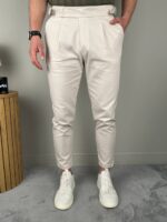 Krem elegantne muške pantalone sa podesivim pojasom, model u prirodnoj svetlosti enterijera