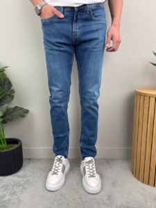Plave muške farmerke produženog modela F6961, model stoji uz zelenu biljku sa rukom u džepu
