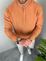 Oker muška košulja sa ruskom kragnom na modelu, ruke u džepovima belih pantalona