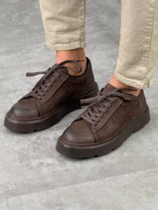 Braon muške kožne cipele Wilson, model čuči pored, beli chunky đon, krem pantalone