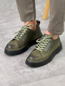Maslinasto zelene muške kožne cipele Tony u prednjem kadru, model u bež pantalonama