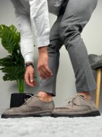 Krupni profil muške cipele sive boje sa belim pertlama uz nogu modela u zelenim pantalonama