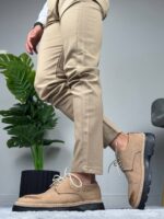 Model u beloj košulji i bež pantalonama nosi muške cipele bež boje, prekrštene noge
