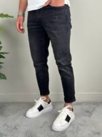 Frontalni kadar muških farmerki F2510 u crnoj boji uz zelenu biljku, beli sneakeri ispod