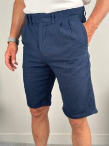 Frontalni kadar muški laneni šorc teget boje, model u beloj majici sa rukama uz telo