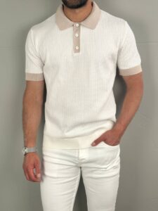 Bela old money polo majica pletena na modelu, frontalni stojeći kadar uz svetlu zidnu pozadinu