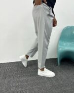 Sive oversize muške pantalone iz polu-profila u pokretu, sužene nogavice nad belim patikama