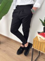 Model u crnim elegantnim pantalonama sa podesivim pojasom, ruka u džepu pored stolice