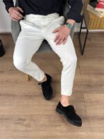 Krem elegantne muške pantalone sa podesivim pojasom, opušten stav modela u enterijeru
