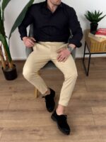 Krem elegantne muške pantalone sa podesivim pojasom, frontalni kadar pored drvene stolice