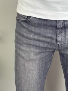 Krupni detalj prednjeg džepa i sive denim teksture klasičnih muških farmerki sa elastinom
