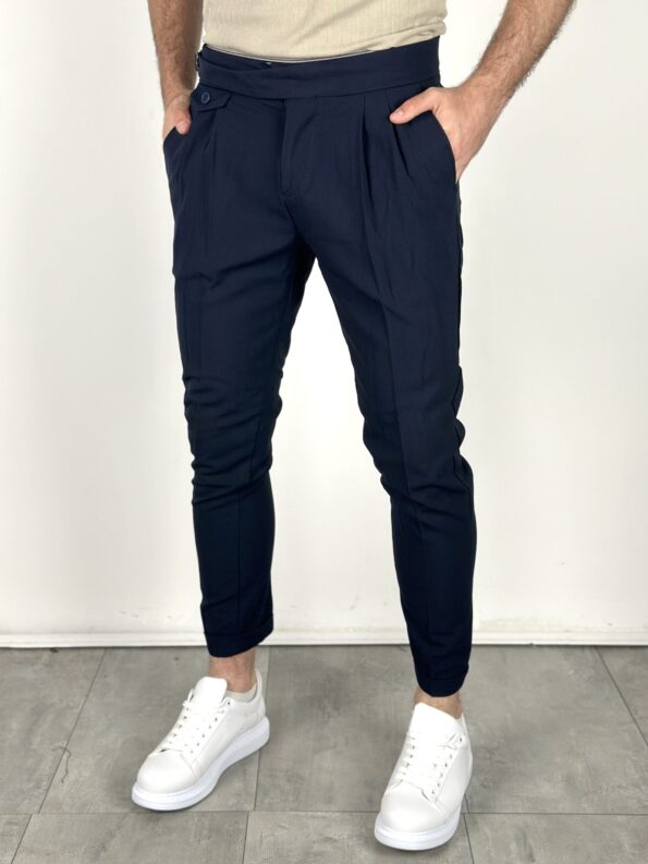 Teget elegantne pantalone sa naborima u struku, prednji kadar, ruke u džepovima i bele patike